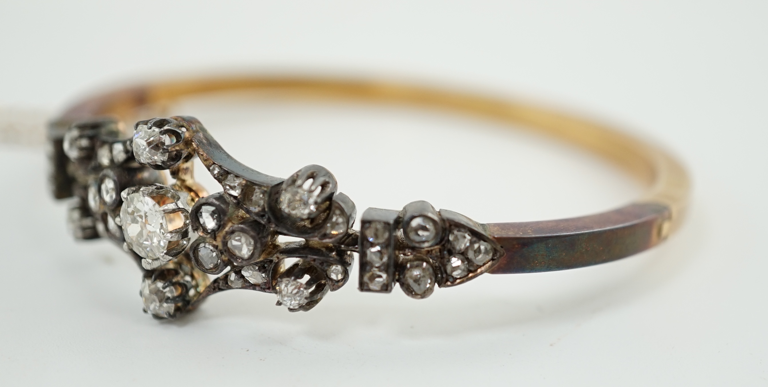 A late 19th/early 20th century French 18ct gold, silver, rose and round cut diamond cluster set hinged bangle